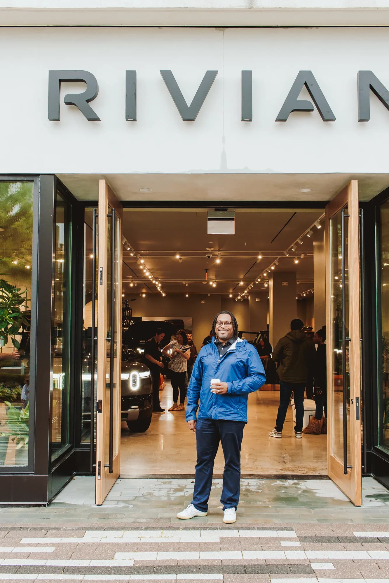 A guest steps out of the Rivian Chicago showroom holding a thrd coffee cup