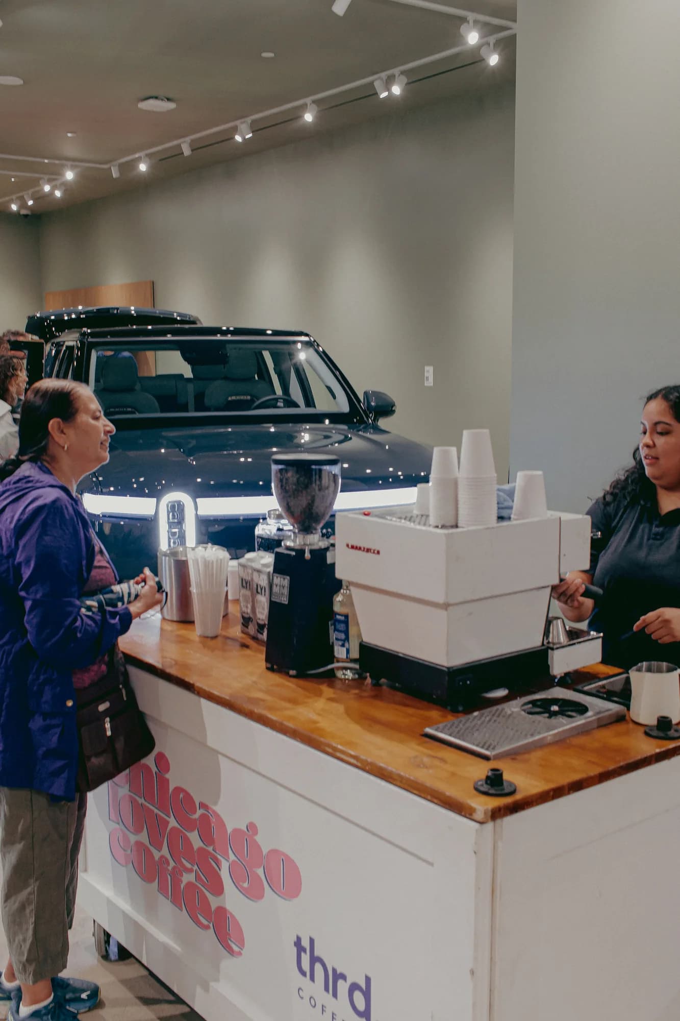 A thrd coffee barista serving a guest at the cart in the Rivian showroom