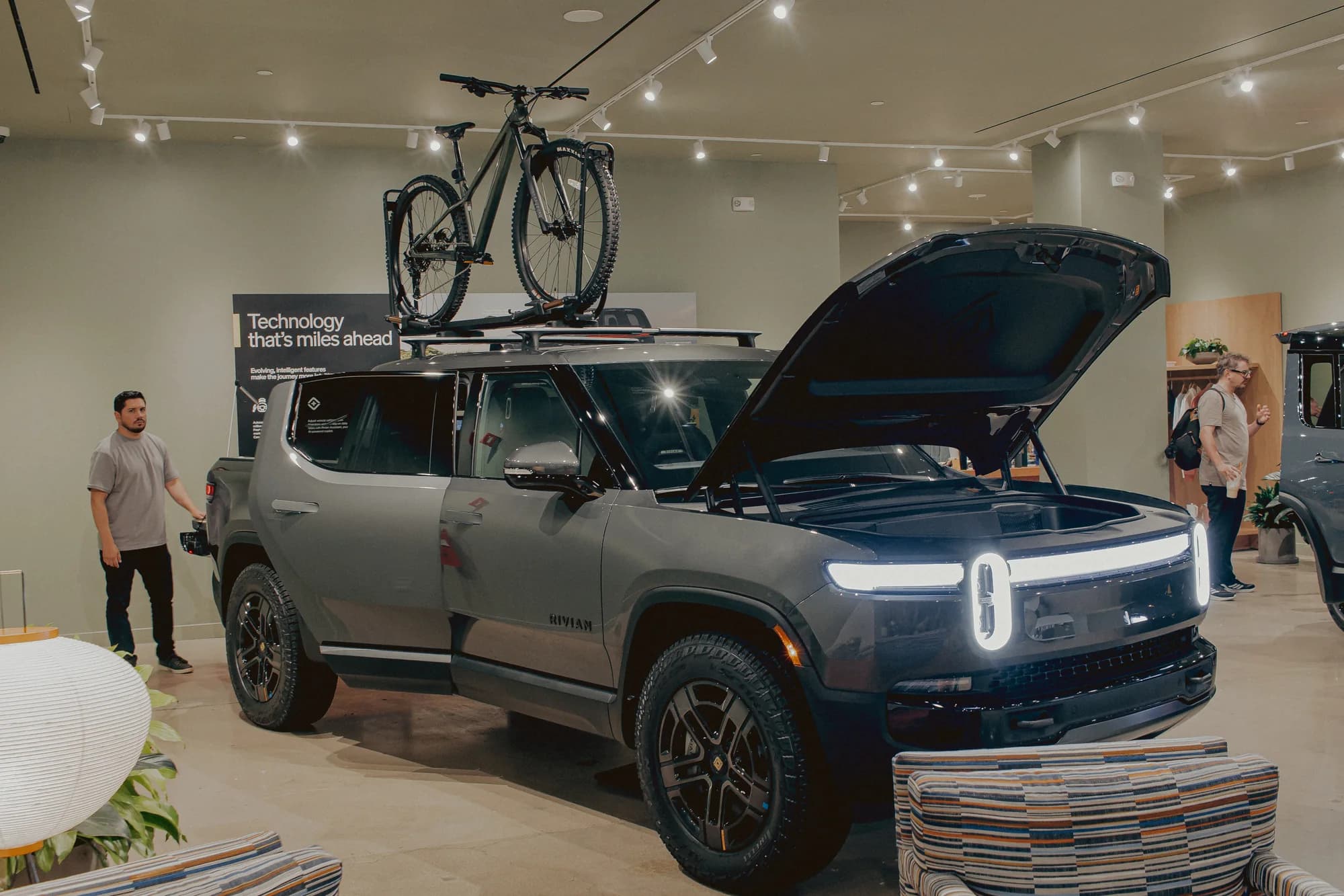 A Rivian R1T on display with a mountain bike on the roof rack and the front trunk open